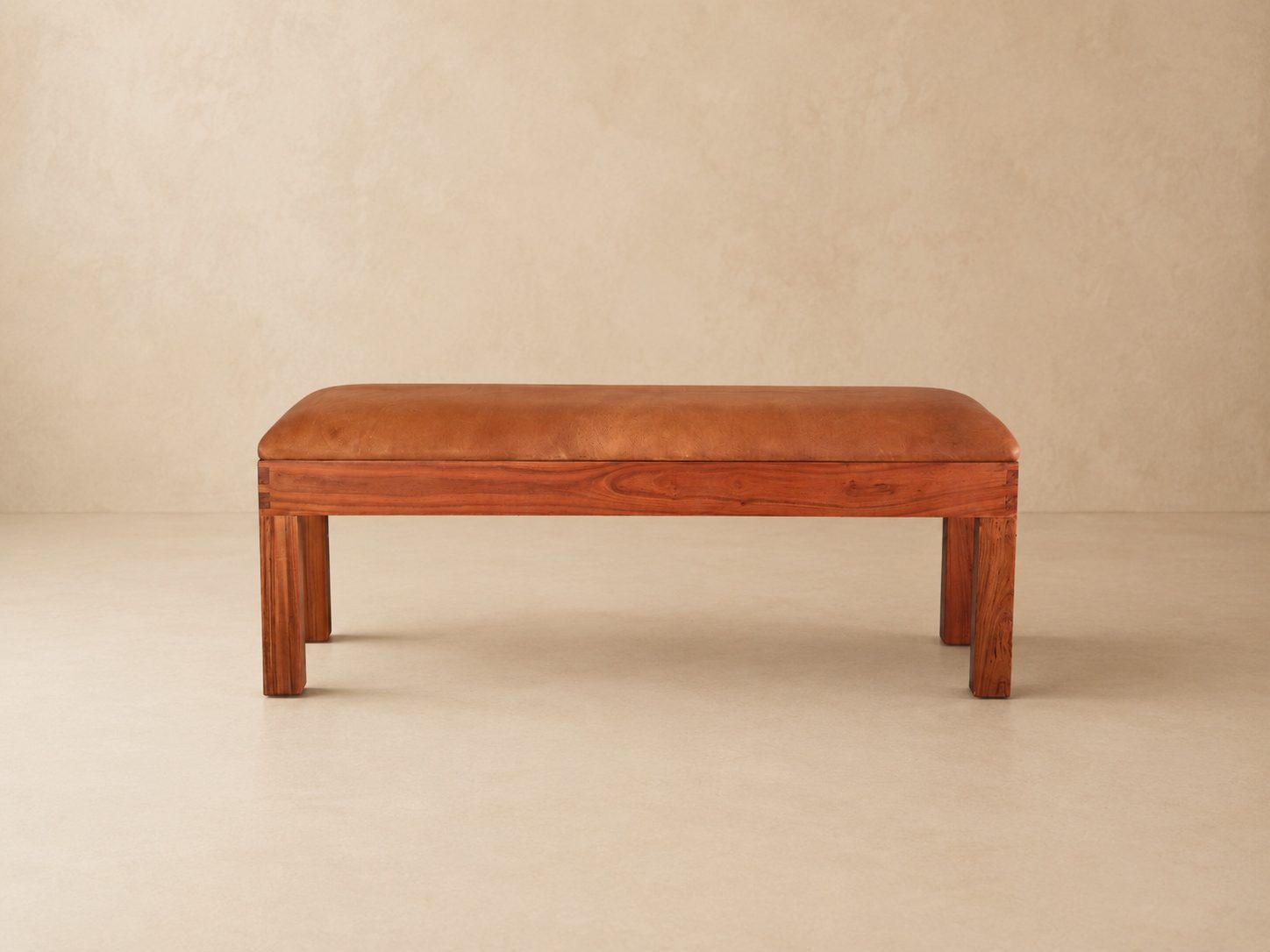 Burchell Upholstered Leather Bench 3 Burchell leather bench with tan upholstered cushion and solid wooden frame on a warm beige studio background.
