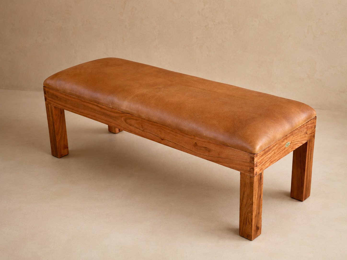Burchell Upholstered Leather Bench 5 Front end view of the Burchell leather bench showing the tan leather cushion, wooden legs and African Touch badge.